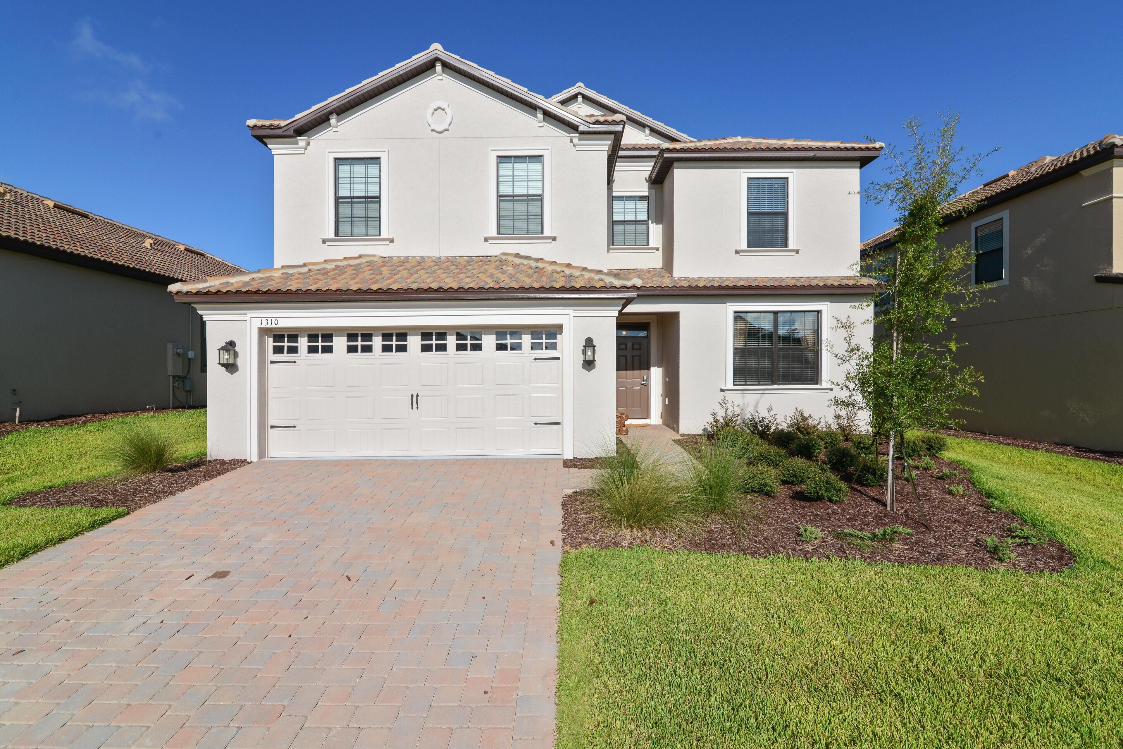 A two-story house with a white garage door, a brick driveway, and a well-maintained lawn.