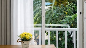 Une pièce avec une fenêtre, une table en bois, une chaise blanche et une plante en pot aux fleurs jaunes.