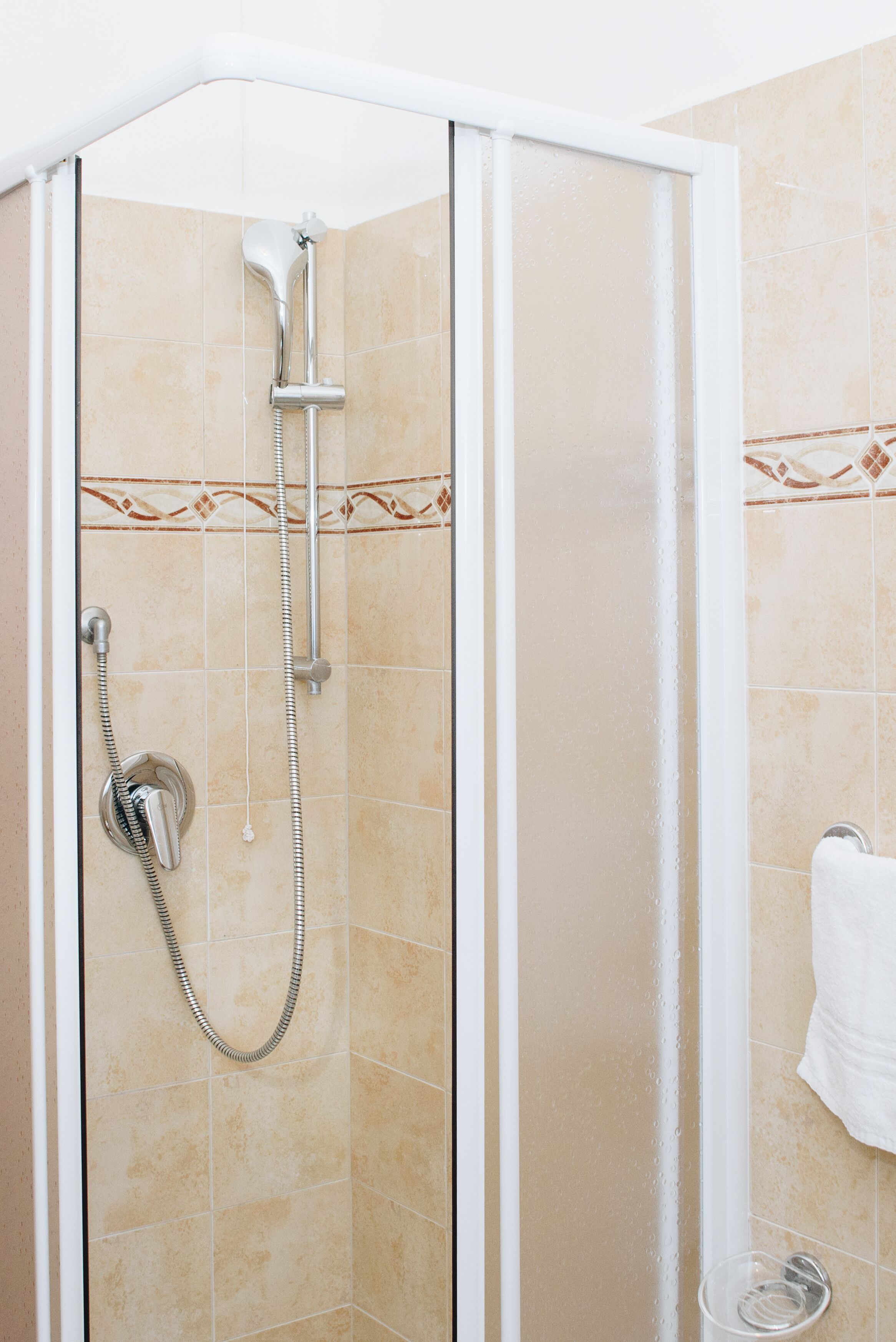 A glass-enclosed shower with beige tiles and a decorative border.