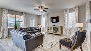 A spacious living room with a sectional sofa, a coffee table, a chair, a TV, and a ceiling fan.