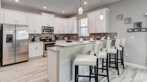 A modern kitchen with white cabinets, stainless steel appliances, a granite countertop, and a bar area with bar stools.
