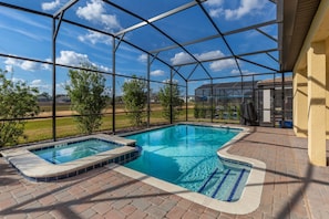 A covered swimming pool with a hot tub, surrounded by a metal frame and brick flooring.