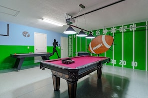 A pool table with a red felt surface, a billiards cue, and a pool ball. There is a green wall with white numbers and a door.