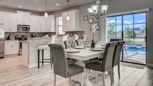 A modern kitchen with white cabinets, a central island, and a dining area with grey upholstered chairs.