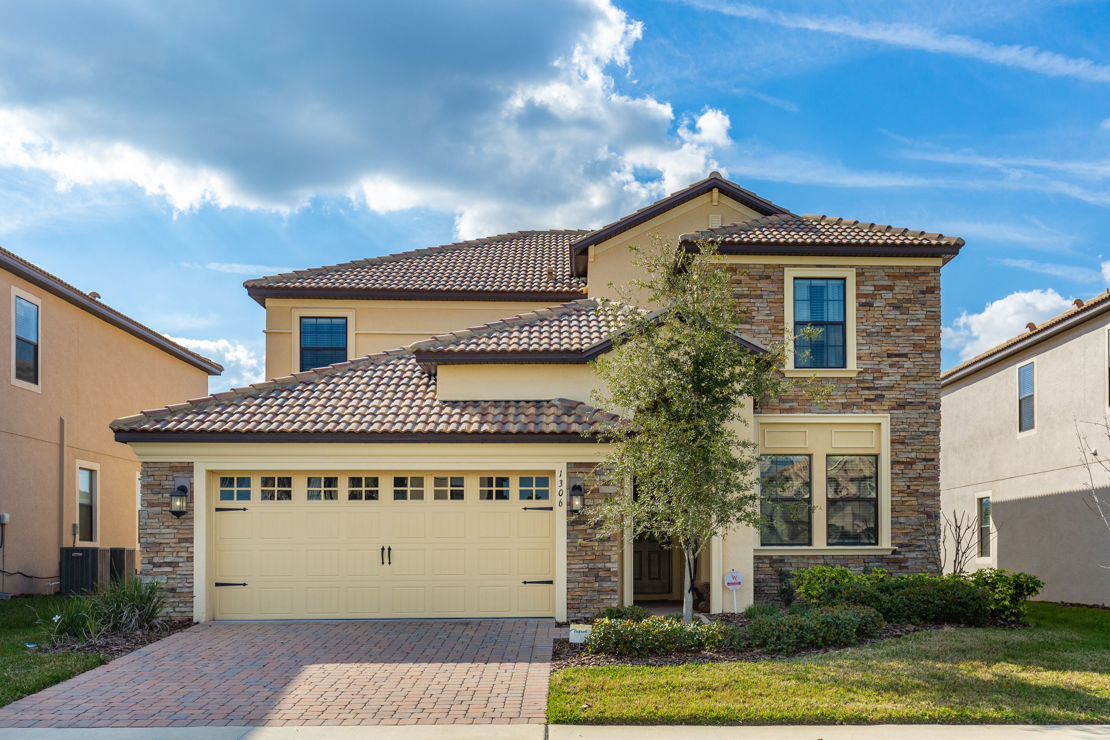 A two-story house with a beige garage door, a stone facade, and a tiled roof.