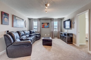 A living room with a sectional sofa, an ottoman, a flat-screen TV, and artwork on the walls.