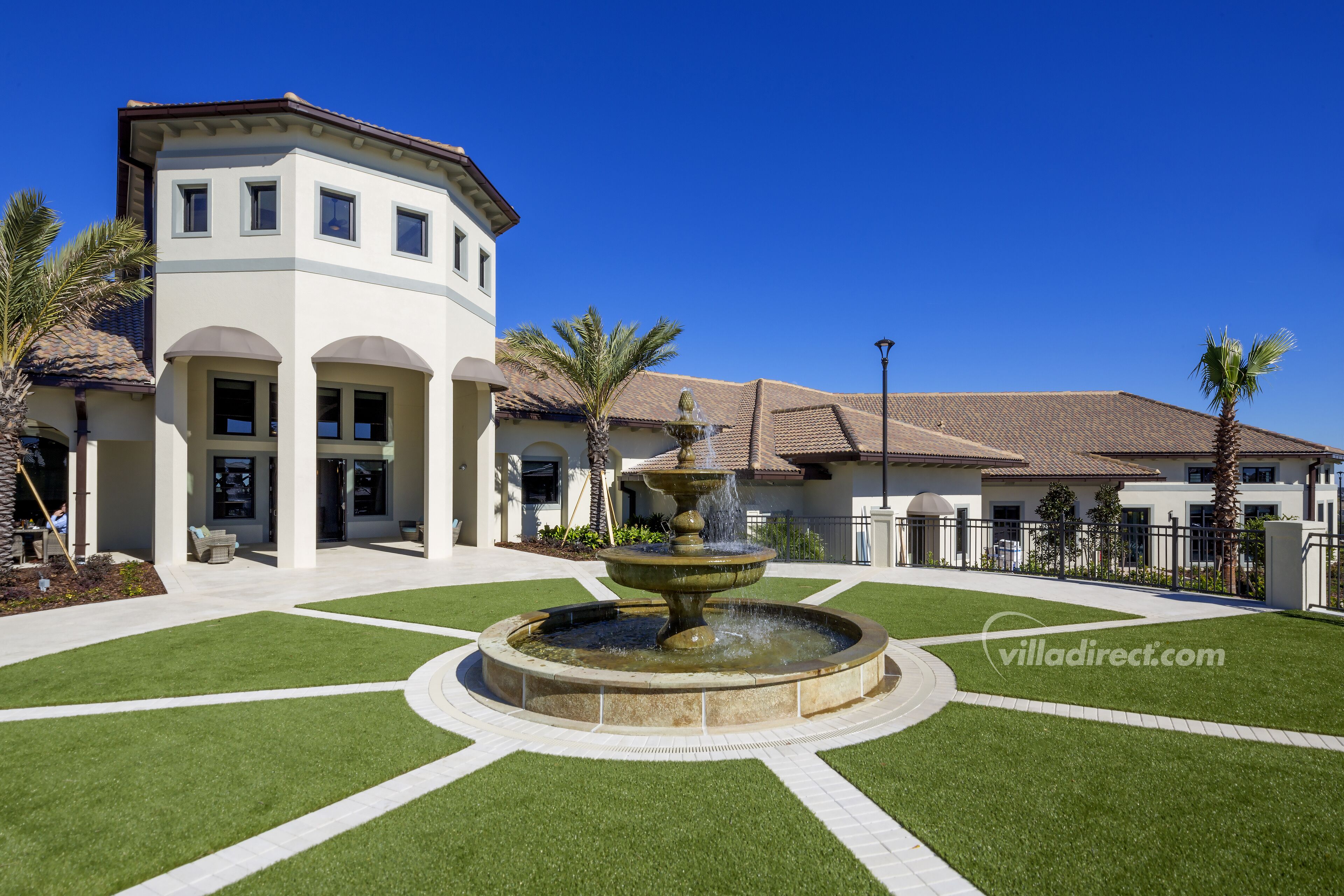 A modern building with a central fountain, surrounded by well-maintained lawns and palm trees.