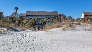 Ett hotell vid stranden med flera våningar, en sandstrand i förgrunden och palmer.