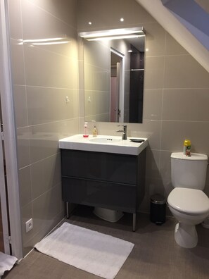 A modern bathroom with a white sink, dark vanity, and a toilet. - Un Figuier Dans Notre Jardin (Beaune-la-Rolande)