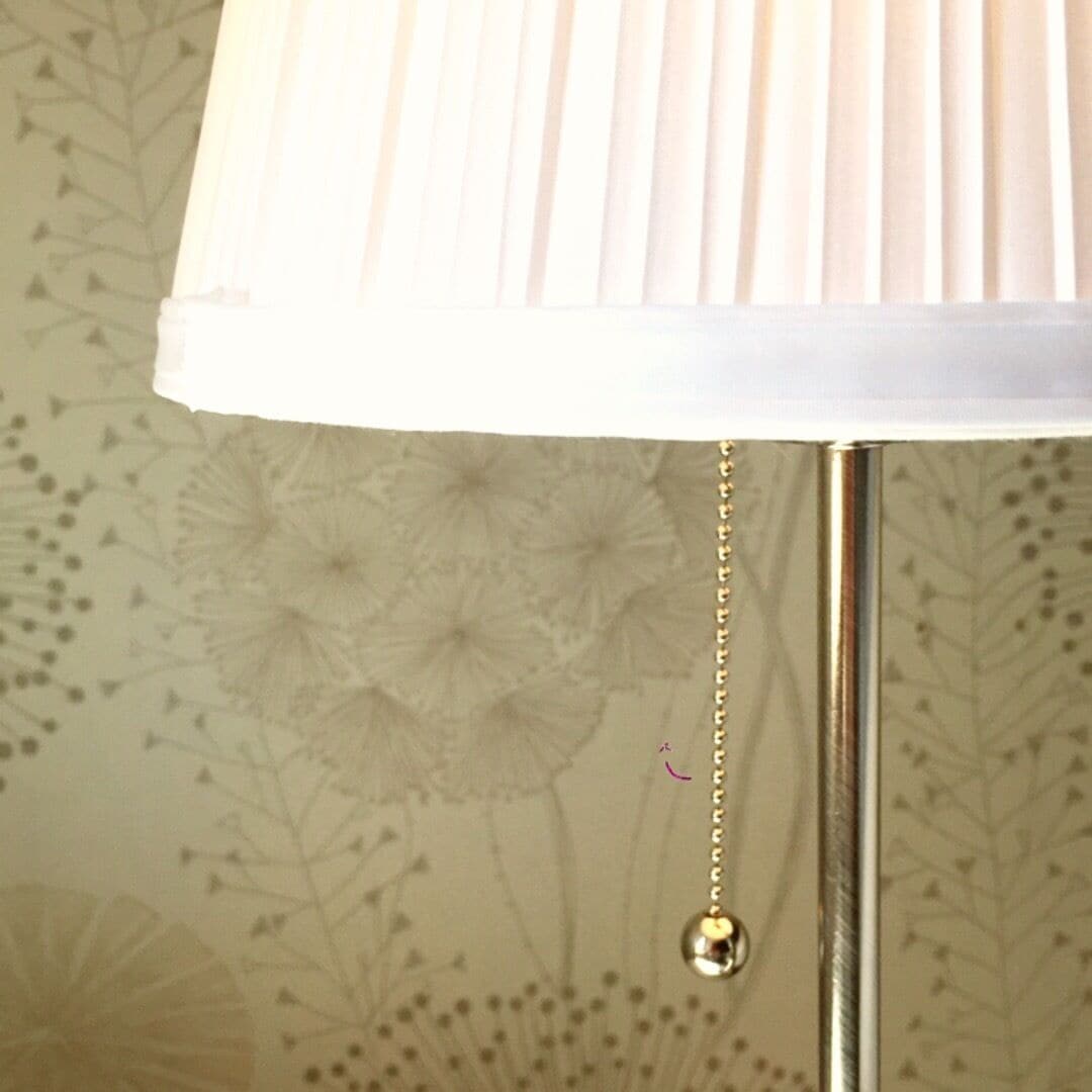 A lamp with a white shade and a hanging ornament.