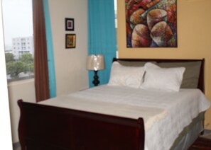 Una cama con cabecera de madera, una lámpara de noche y un cuadro en la pared.