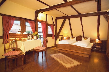 A traditional room with a wooden bed, a dining table with chairs, and a window with curtains.. Hotel Restaurant Zum Nachtwächter