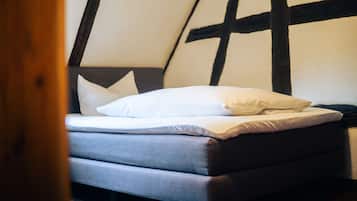 Ein Bett mit weißem Kopfkissen und grauem Matratzenkern in einem Zimmer, das ein dunkles Holz-Kopfteil und eine weiße Wand aufweist.