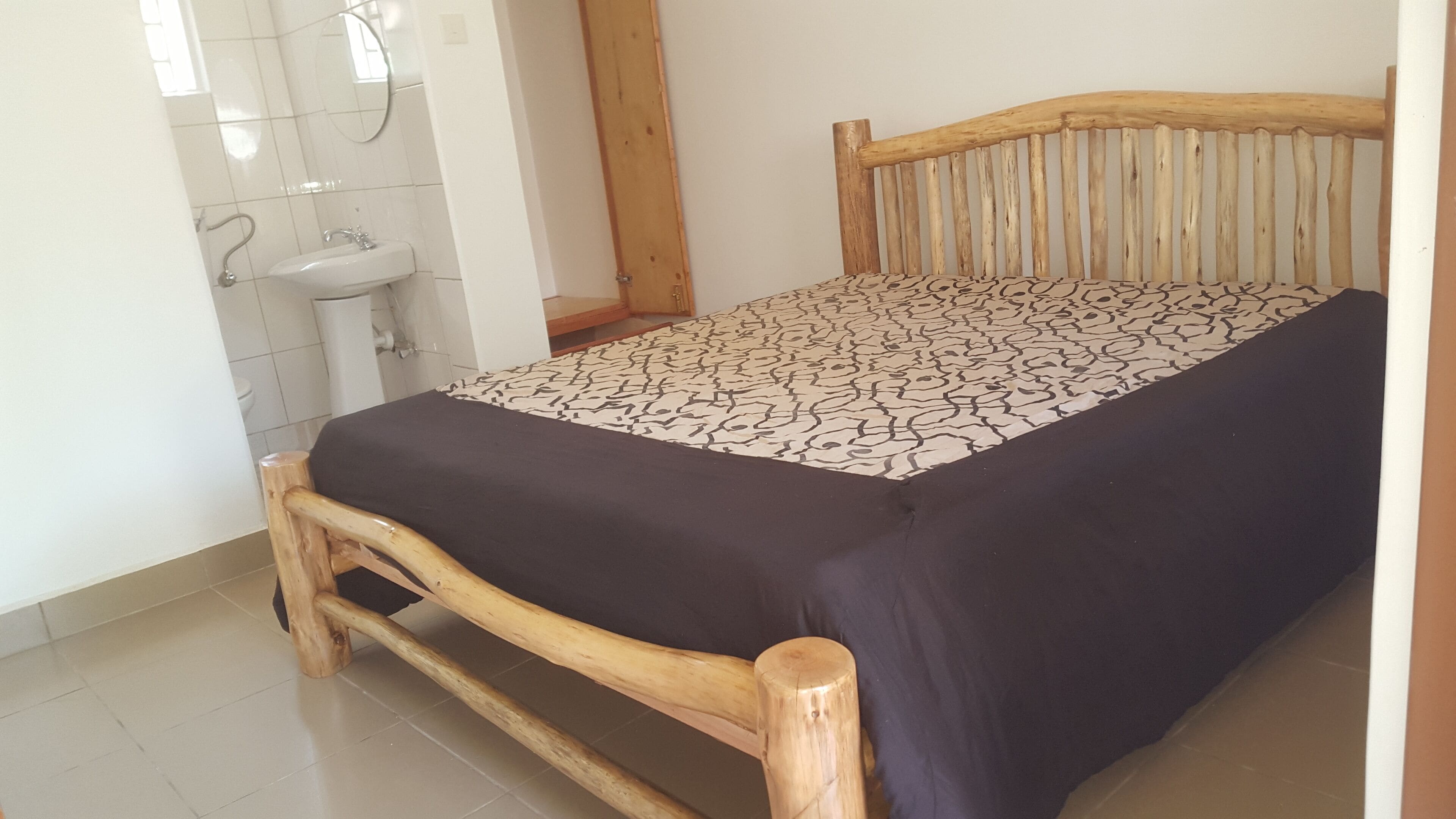 A wooden bed with a patterned bedspread, a wooden headboard, and a white sink in a bathroom.