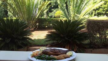 Un plato de comida con pescado, verduras y rodajas de lima en un balcón con vista a un jardín.