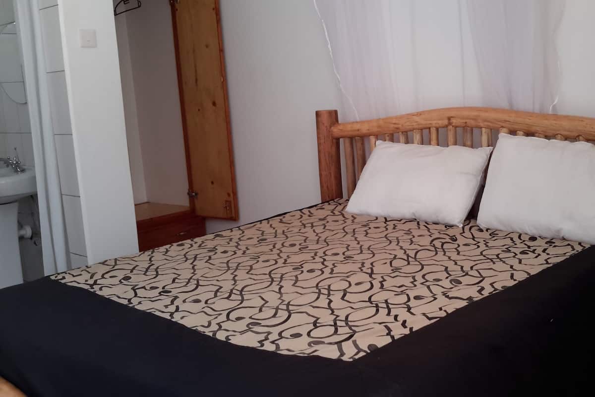 Una cama con colcha estampada y dos almohadas, cabecera de madera y una pequeña mesa auxiliar al lado.