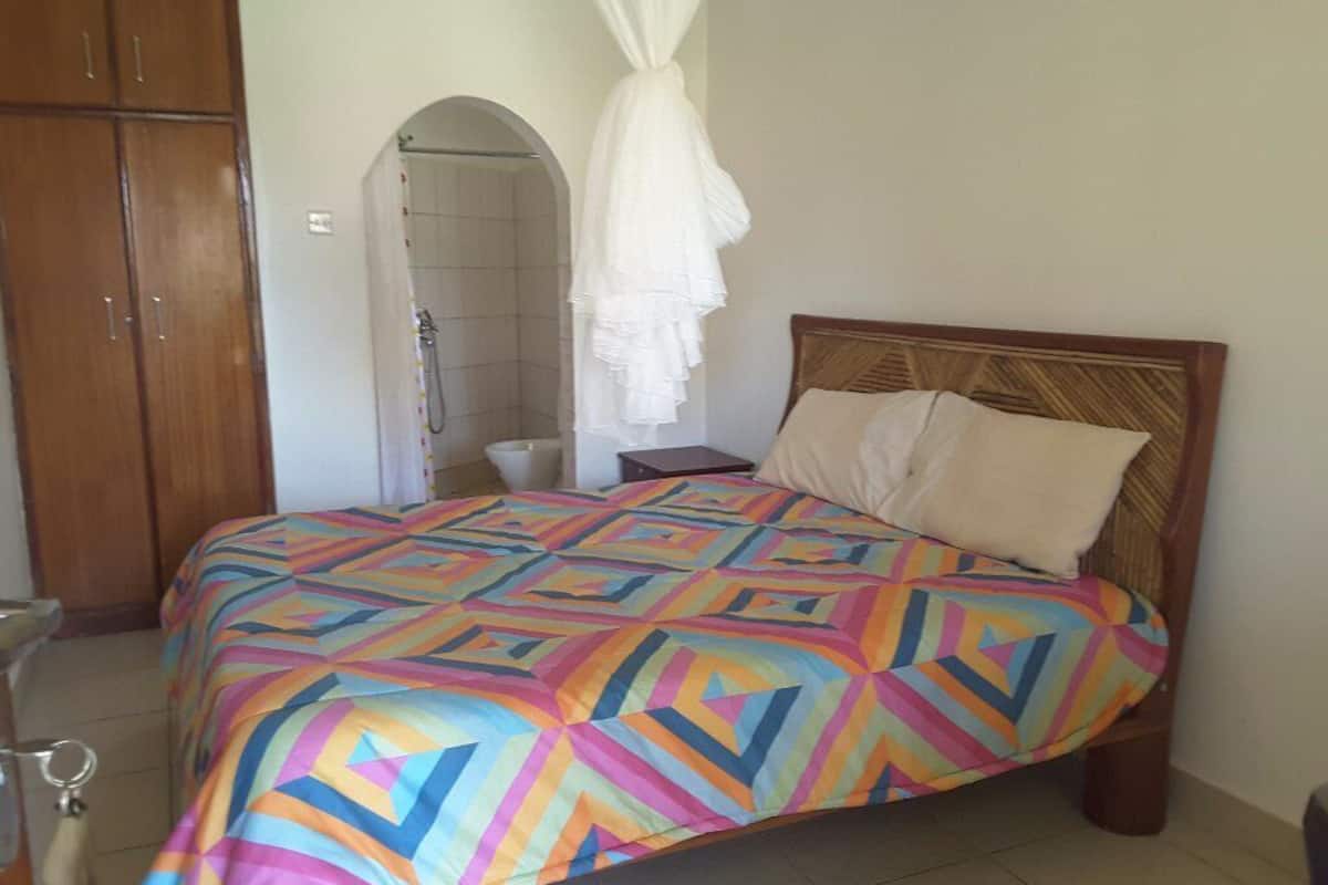 Un dormitorio con una colcha de colores, un cabecero de madera, un dosel blanco y un armario de madera.