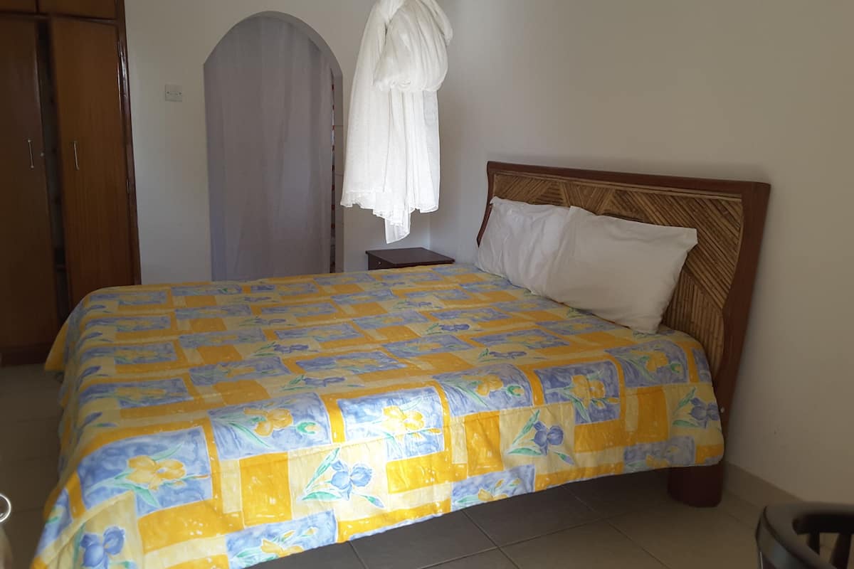 Un dormitorio con cama, armario de madera y cortina blanca.