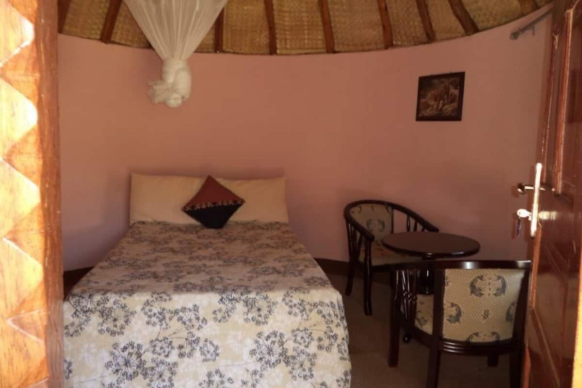 Un dormitorio con una cama, una mesita de noche, una silla y un mosquitero sobre la cama.
