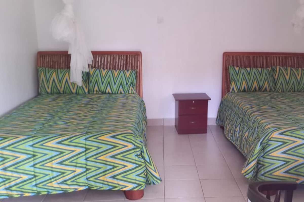 Una habitación con dos camas, cada una con una colcha estampada, una mesita de noche de madera y suelo de baldosas.
