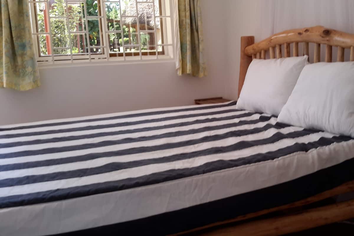 Una cama con estructura de madera, ropa de cama a rayas y dos almohadas.