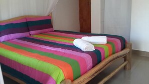 Uma cama com um edredom colorido listrado e duas toalhas enroladas sobre ela.