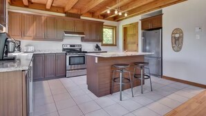 A modern kitchen with wooden cabinets, a central island with stools, stainless steel appliances, and a wooden ceiling. - Dreaming unit near Le Massif (Petite-Rivière-Saint-François)