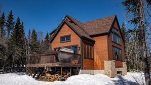 A two-story wooden house with a deck, surrounded by snow and trees. - Dreaming unit near Le Massif (Petite-Rivière-Saint-François)