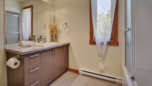 Ein modernes Badezimmer mit Waschtisch, Spiegel, Toilettenpapierhalter und einem Fenster mit transparenten Vorhängen.