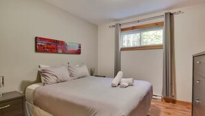Ein Schlafzimmer mit Bett, Nachttisch, Kommode, einem Fenster mit Vorhängen und einem Bild an der Wand.