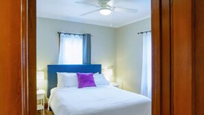 Quarto de hotel com cama, ventoinha no teto e janela com cortinas.
