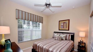 A bedroom with a bed, a ceiling fan, a window with blinds, a bedside table, and a lamp. - Dog-Friendly · Dual Masters · Private Pool · Resort Amenities · Near Disney (Kissimmee)