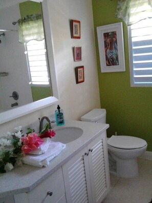 A bathroom with a white sink, toilet, and vanity. There are three framed pictures on the wall and a window with blinds.