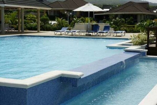 Une piscine dont les bords sont recouverts de carreaux bleus, avec des chaises longues et des parasols.