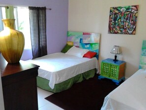 A bedroom with a bed, a nightstand, a lamp, a colorful painting, and a vase on a dresser.
