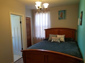 A bedroom with a wooden bed, a chandelier, a door, and a window with curtains.