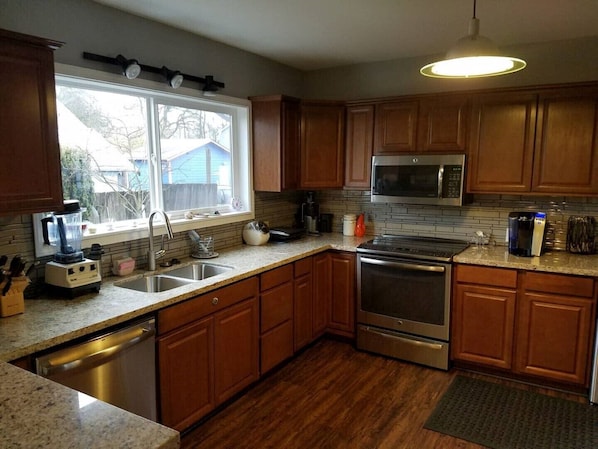 A kitchen with wooden cabinets, a stainless steel stove, a microwave, and a window with a view of a blue house.