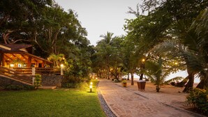 A well-lit pathway leading to a building with a stone facade, surrounded by lush greenery and palm trees. - La Jolla Beach Resort (Bagac)