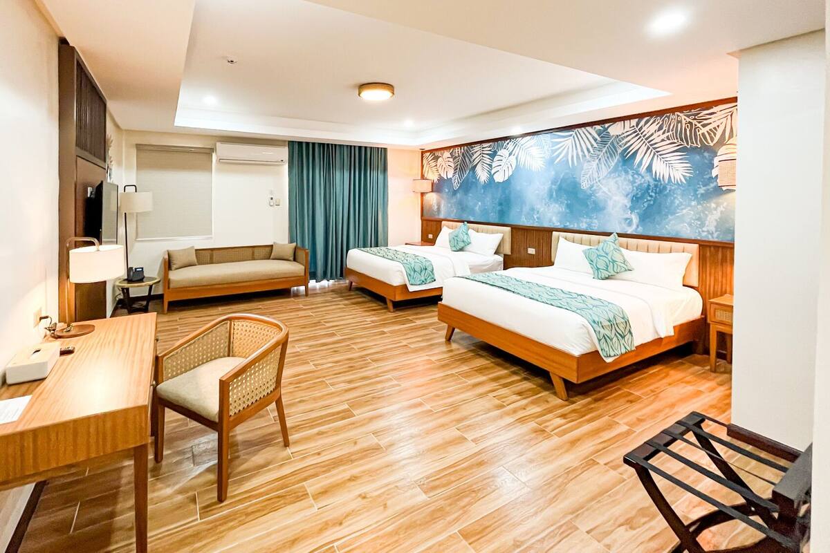 A hotel room with two beds, a sofa, a desk, and a chair.