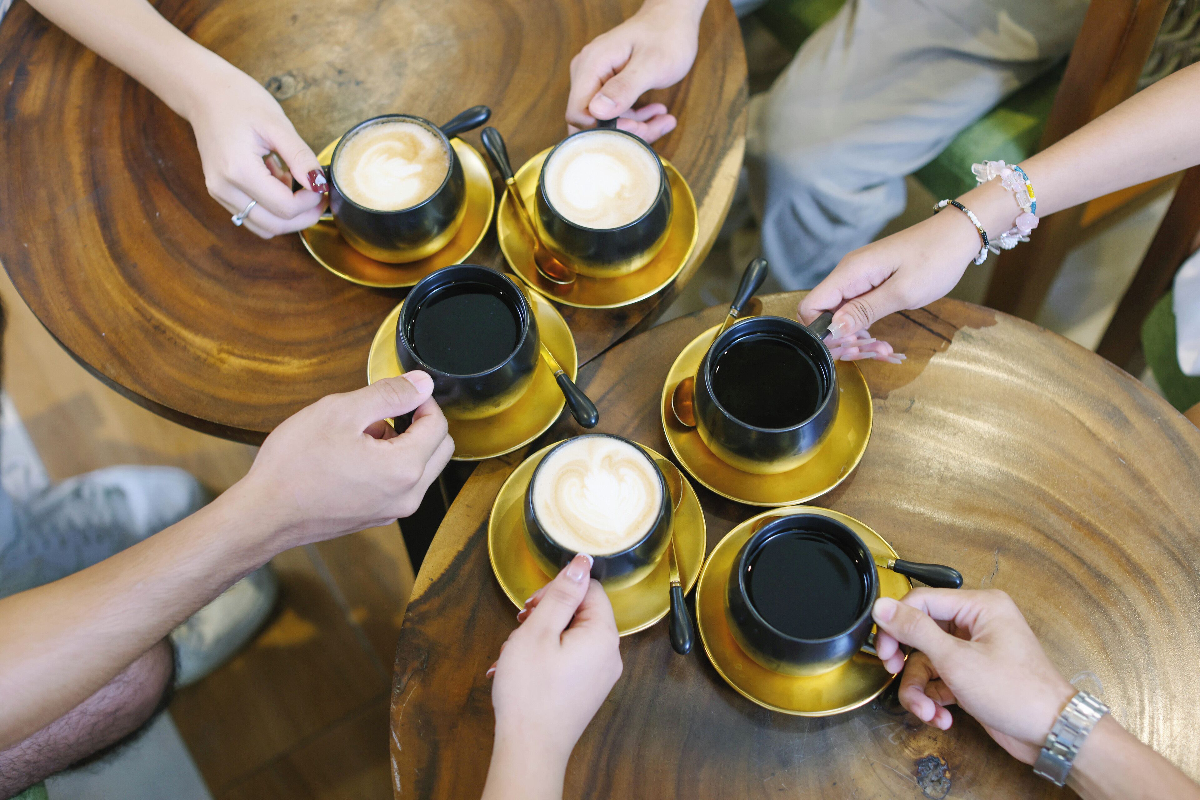 A group of people holding coffee cups around a wooden table.