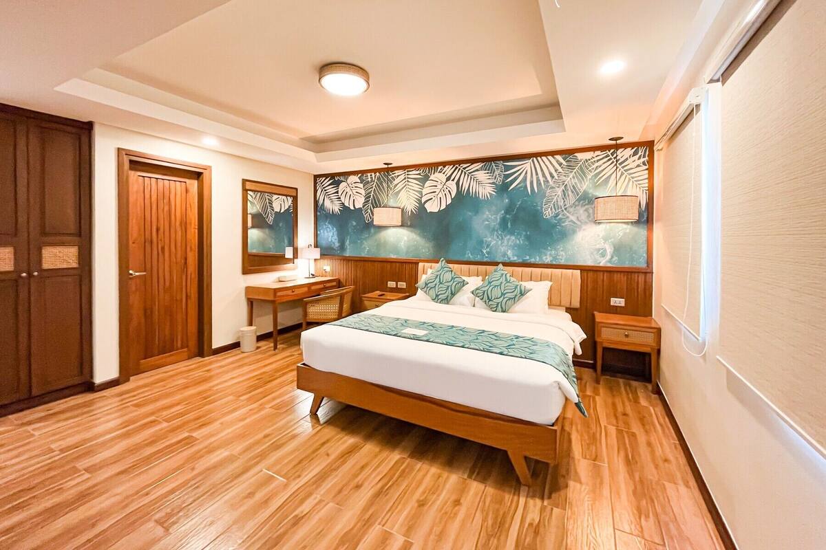 A junior suite room with a wooden bed, a desk, a chair, and a large mirror.