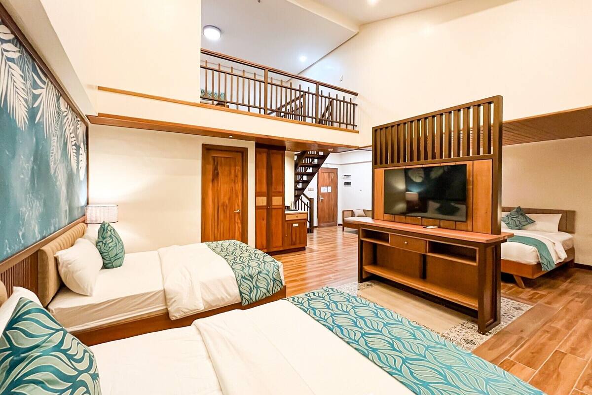 A family room with loft, featuring two beds, a TV, and a staircase.