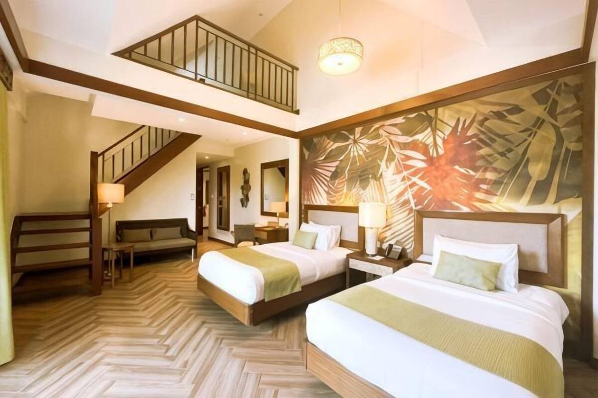 A hotel room with two beds, a staircase, a large wall mural, and a wooden floor.