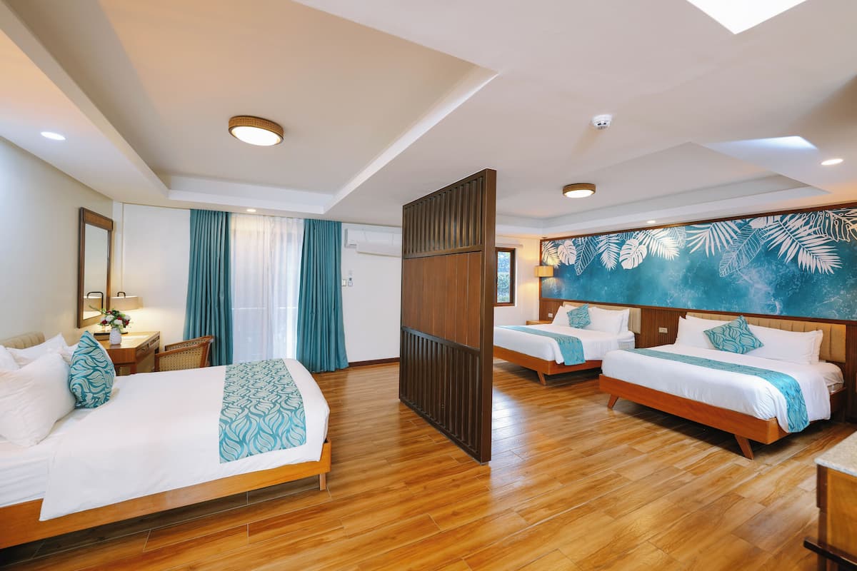 A hotel room with two beds, wooden flooring, a large window with curtains, a desk with a chair, and a wall with a leaf pattern.