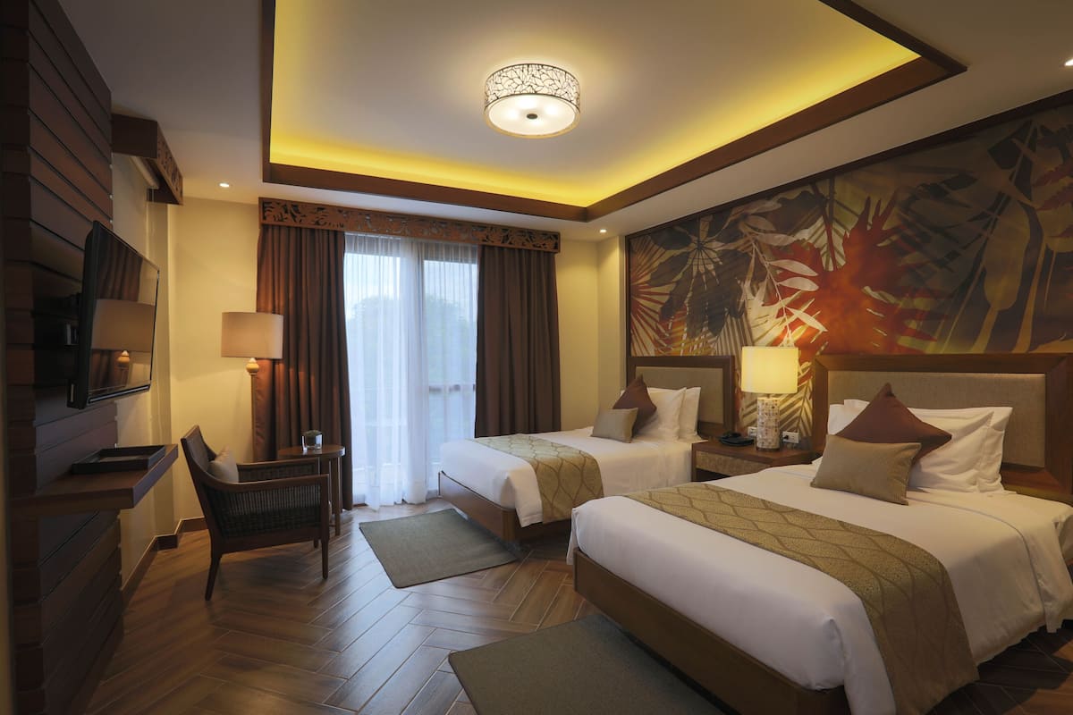A hotel room with two beds, a desk, a chair, a TV, and a large window with curtains.