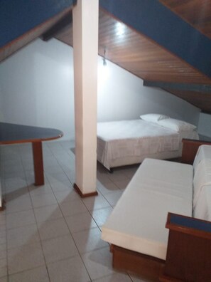 A small, single-room apartment with a sloped ceiling, a bed, a small table, and a bench. - Agua Marinha II (Florianópolis)