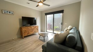 Ein Wohnzimmer mit Flachbildfernseher auf einer Holzkommode, einem grauen Sofa und einem Deckenventilator.