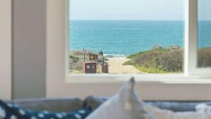 Une vue depuis une fenêtre, avec une plage et une petite construction au loin.