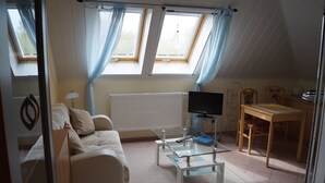A room with a sofa, a glass coffee table, a TV, and a dining area with a table and chairs. - Apartment Hiddensee (Wiek)