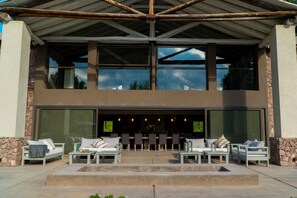 A modern outdoor seating area with multiple sofas and tables, large windows, and a stone wall.